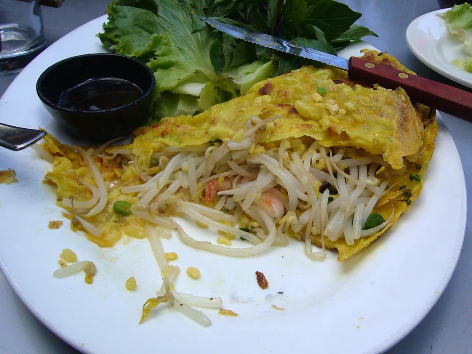 Crisp yellow Vietnamese crêpe filled with shrimp, pork, and sprouts beside herbs