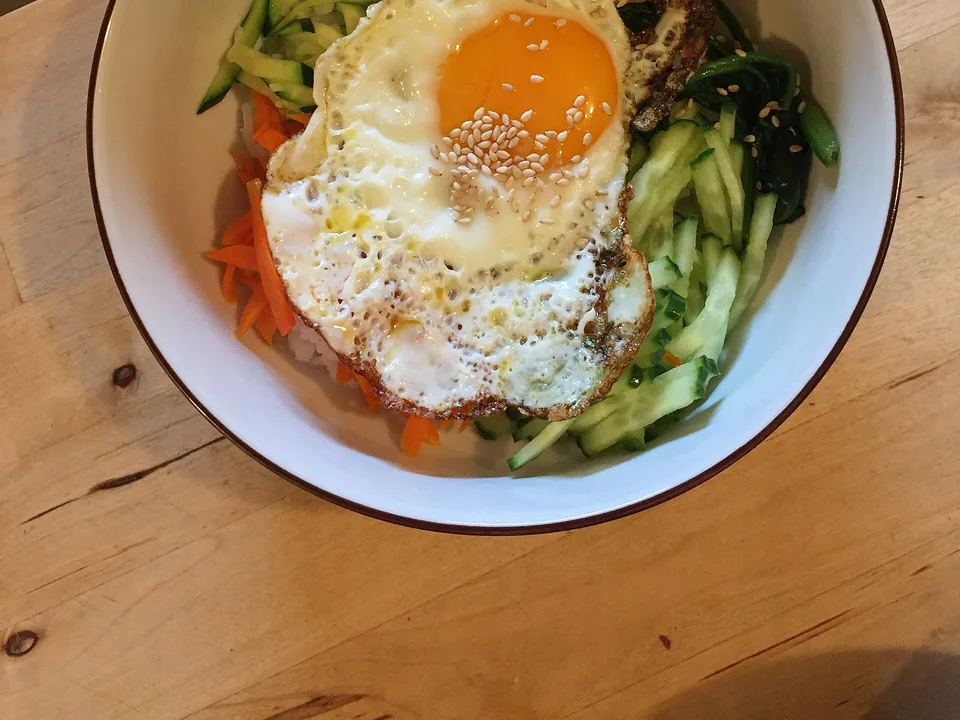 Vegetable bibimbap with separated colourful vegetables and a fried egg over rice
