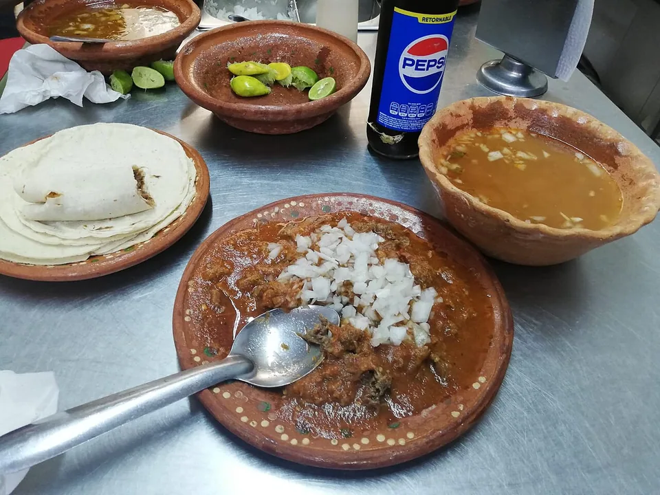 Beef birria in red consommé with onion, cilantro and lime