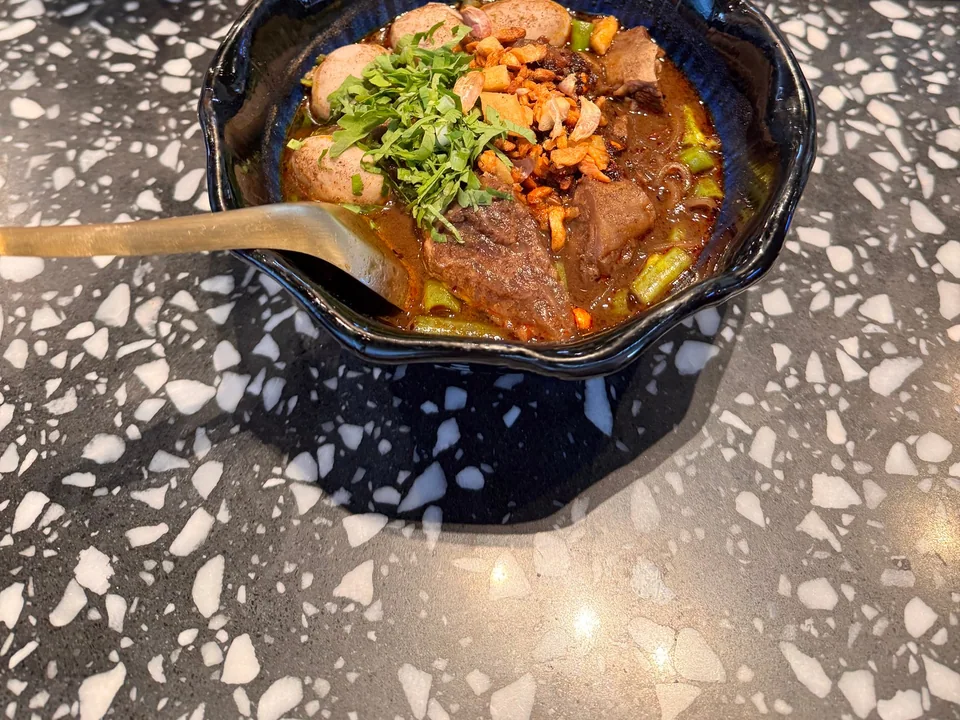 Dark beef boat noodles with rice noodles, sliced shank, beef balls, morning glory, sprouts, basil, celery, and fried garlic