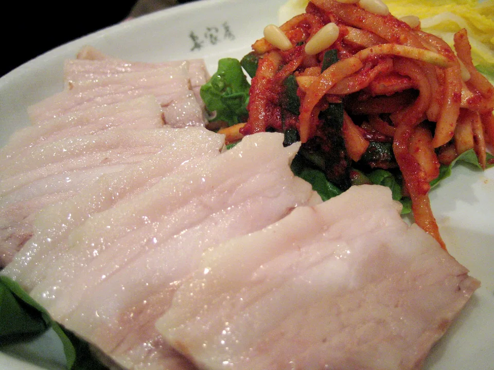 Warm sliced bossam pork beside spicy radish salad, napa, perilla, garlic, and pine nuts