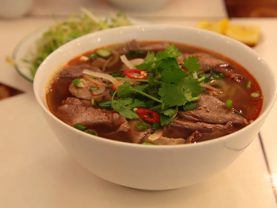 Huế noodle soup with sliced beef, pork hock, round rice noodles and herbs in red broth