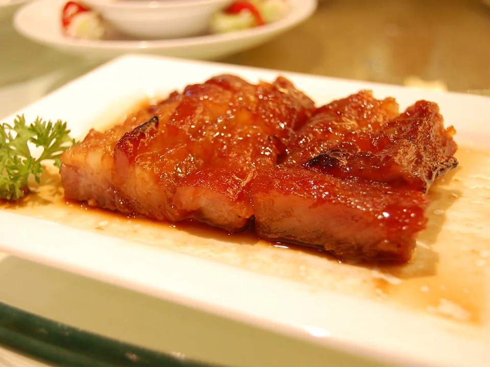 Glossy sliced char siu on a white plate with a small parsley sprig