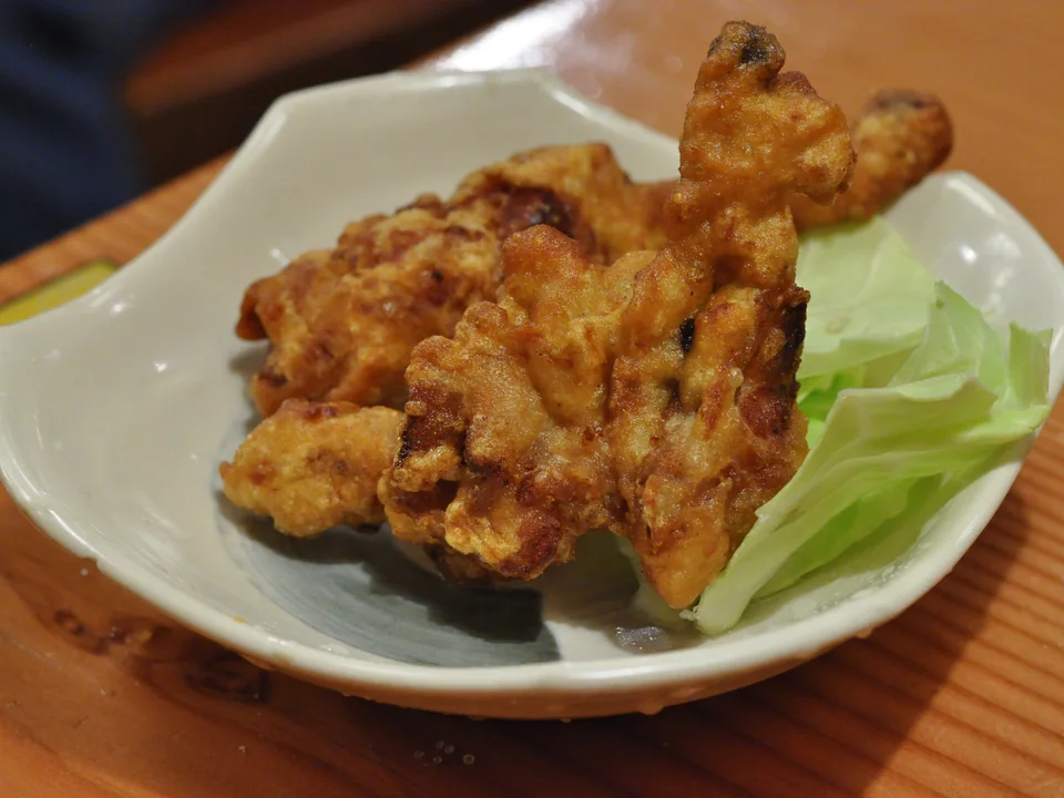 Crisp golden chicken karaage piled on a white plate with raw green cabbage leaves
