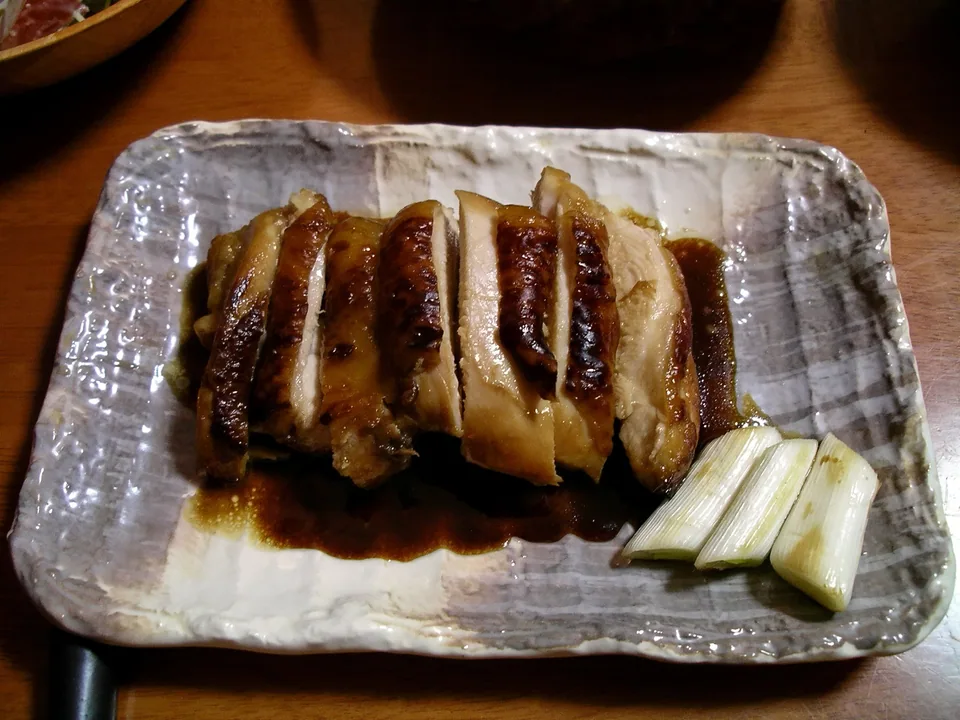 Glossy sliced chicken teriyaki with caramelized skin, sauce, and grilled Japanese long onion