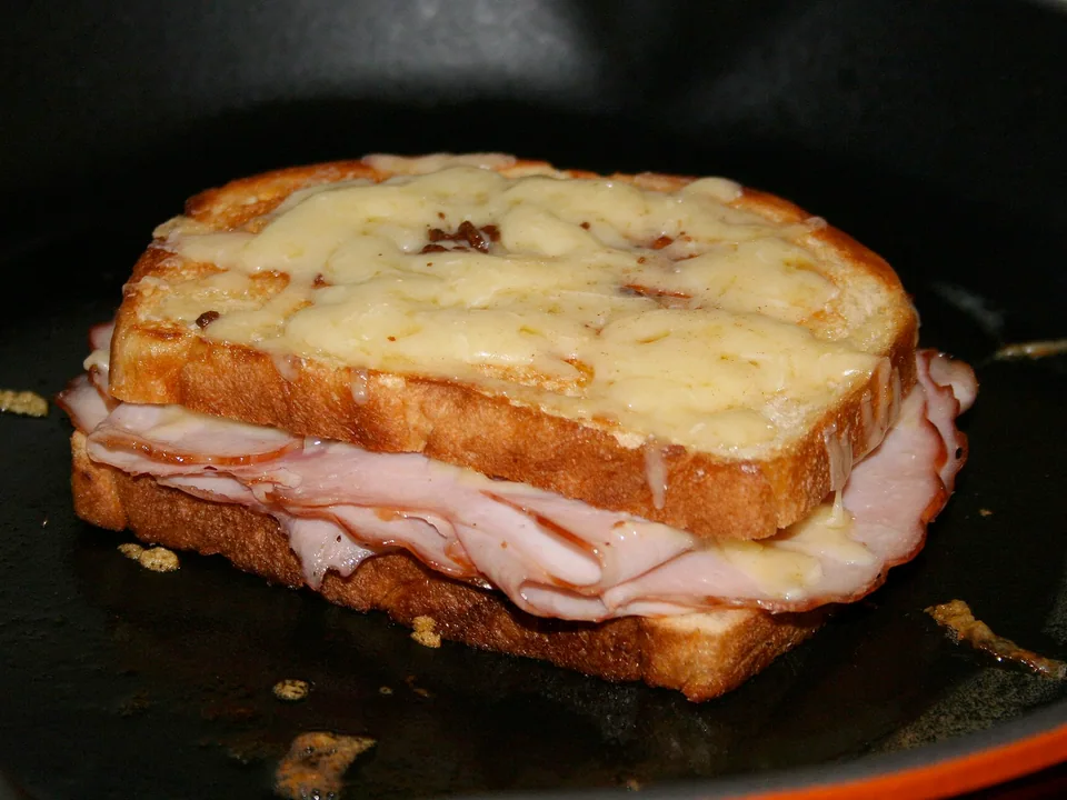 Golden ham sandwich topped with melted cheese and white sauce
