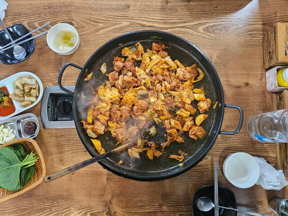Spicy glazed dakgalbi with cooked chicken, cabbage, sweet potato, rice cakes, and perilla
