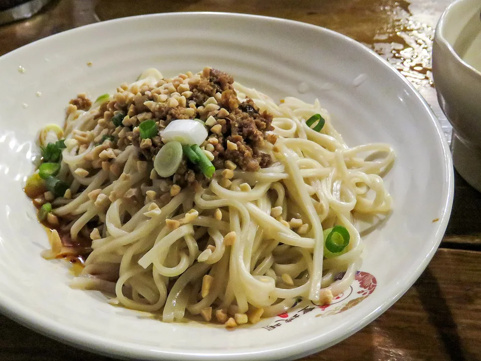 Dan dan noodles coated in sesame-chile sauce with a pork topping, scallions, and crushed peanuts