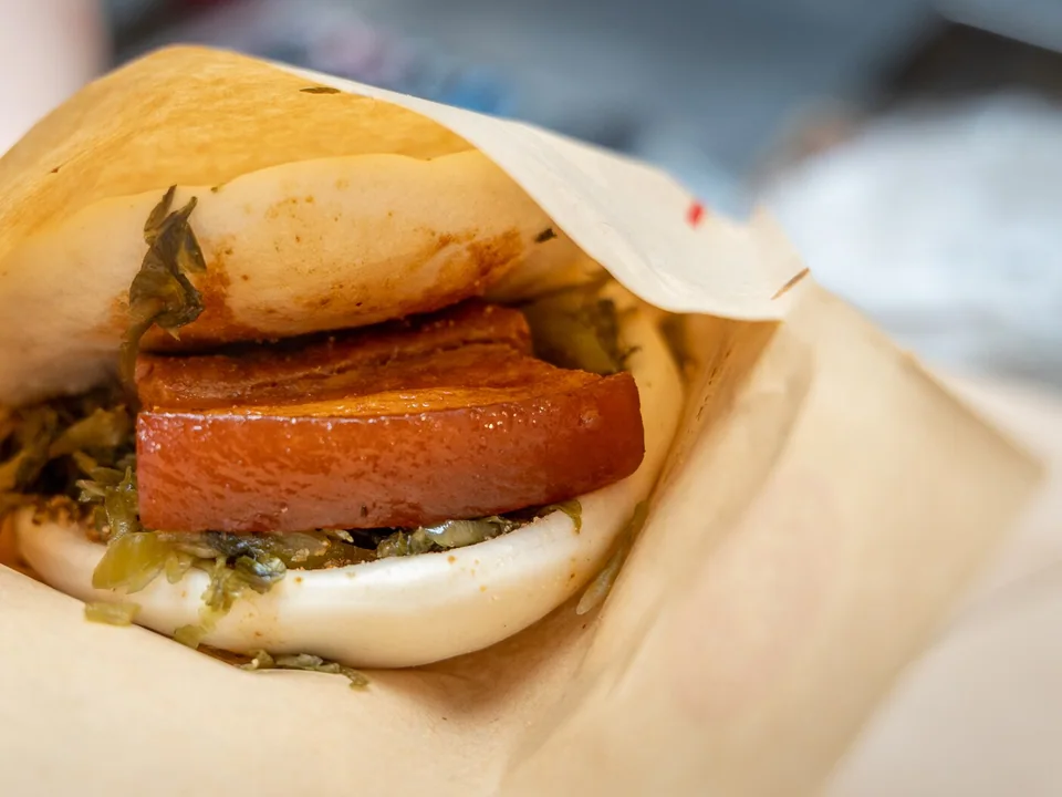 Gua bao filled with braised pork belly, pickled mustard greens, peanut sugar, and cilantro