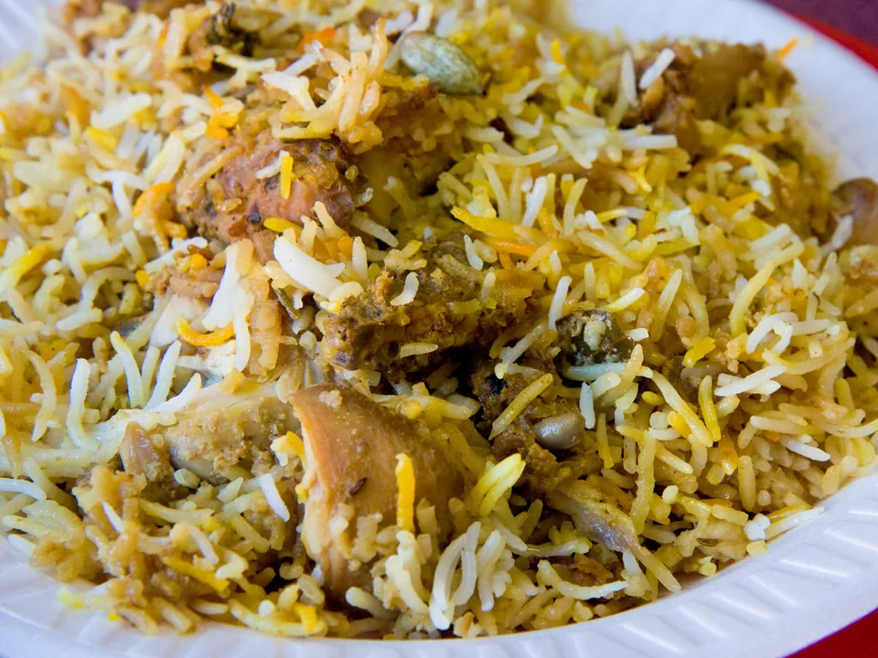 Hyderabadi chicken dum biryani with separate saffron basmati grains, bone-in chicken, fried onions, mint, and cilantro