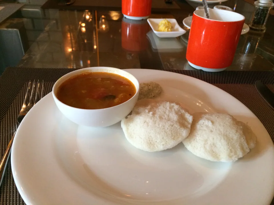 Soft white idli with orange-brown vegetable sambar and white coconut chutney