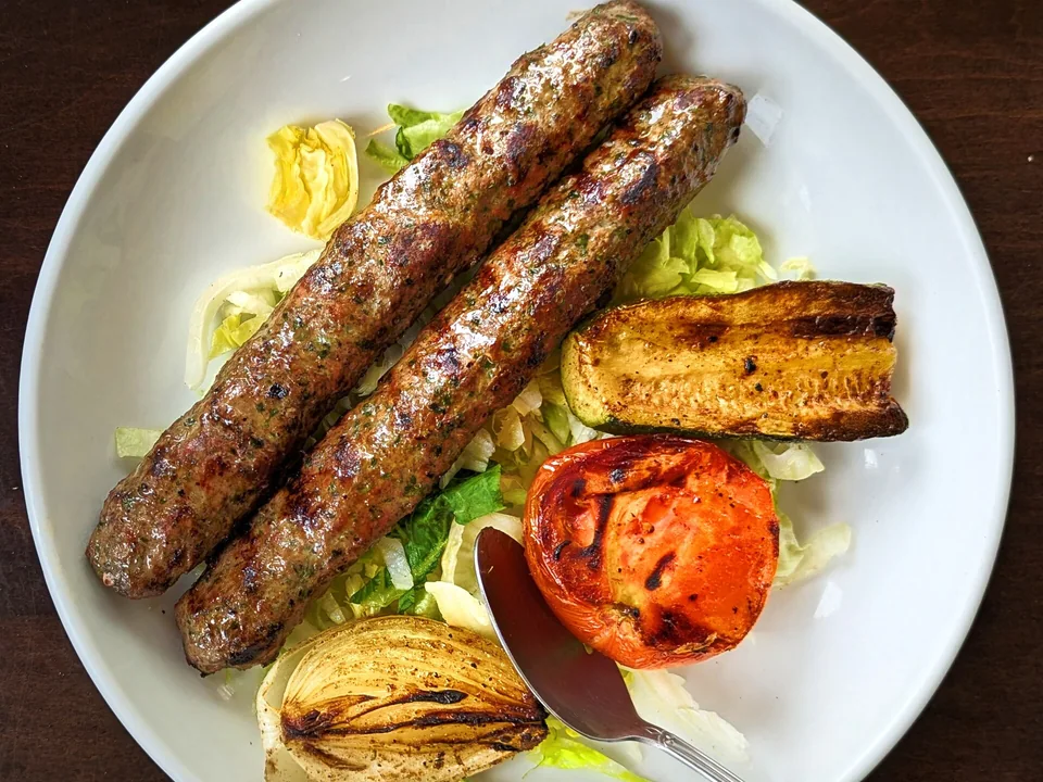 Grilled Iraqi lamb kofta skewers with charred vegetables and yogurt sauce