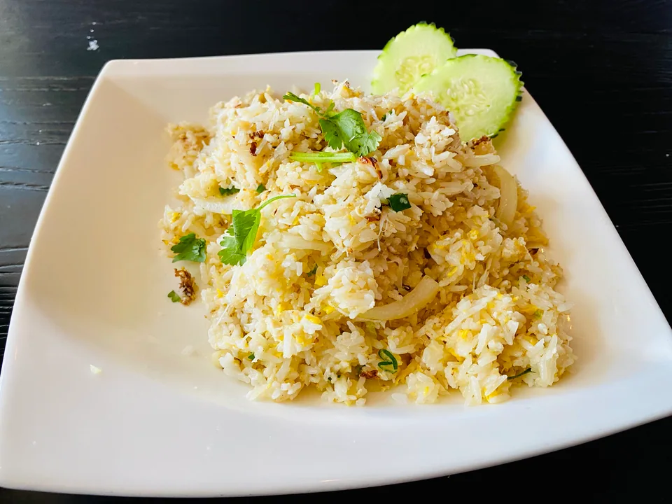 Pale-gold Thai crab fried rice with egg, scallion, cucumber, tomato, and lime