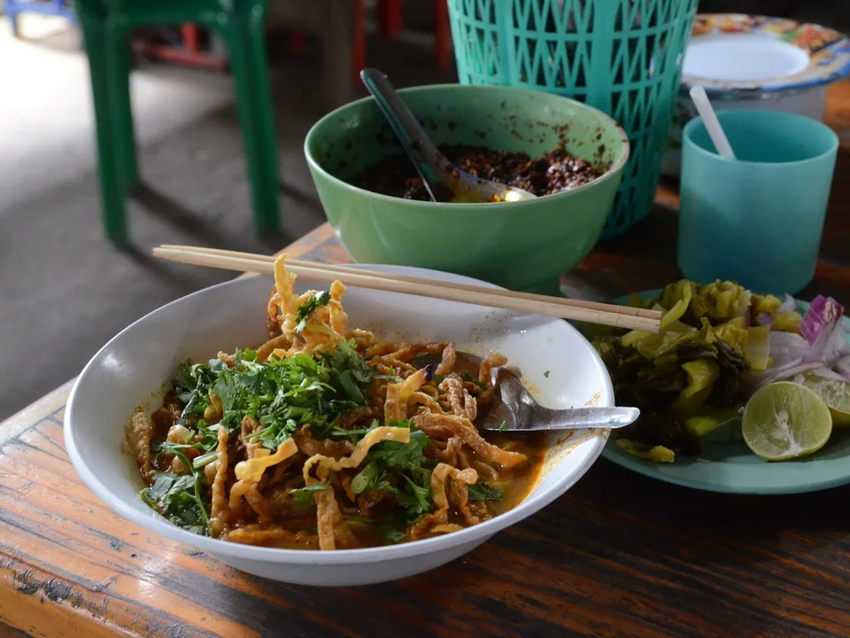 Chiang Mai chicken Khao Soi with a drumstick, coconut curry, boiled egg noodles, crisp noodles, pickled mustard, shallot, and lime