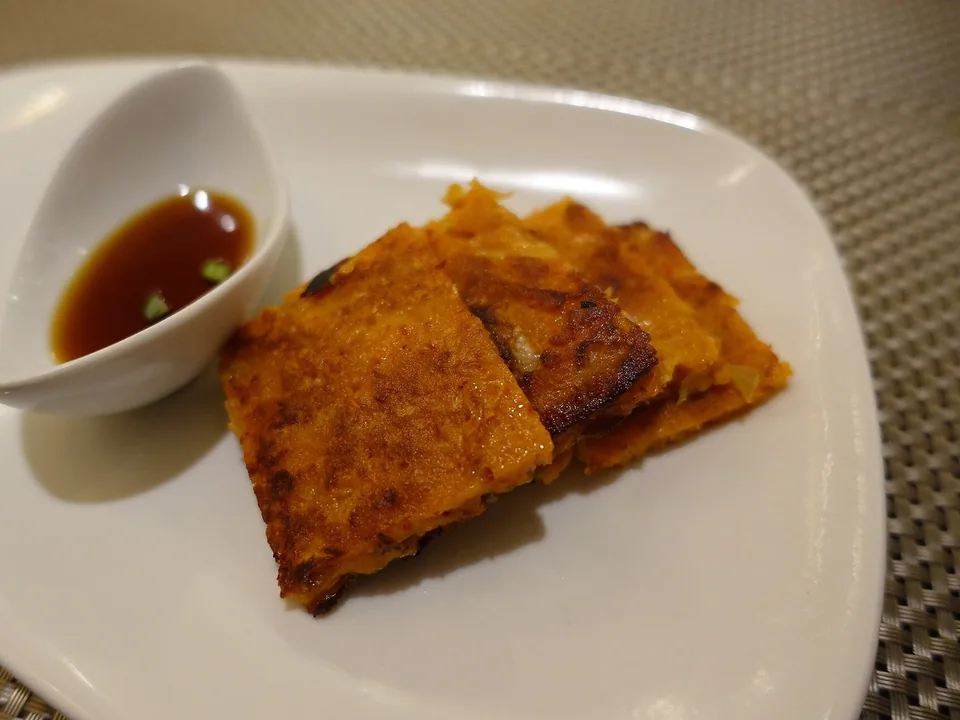 Thin crisp red kimchi pancake cut into pieces beside a dark dipping sauce