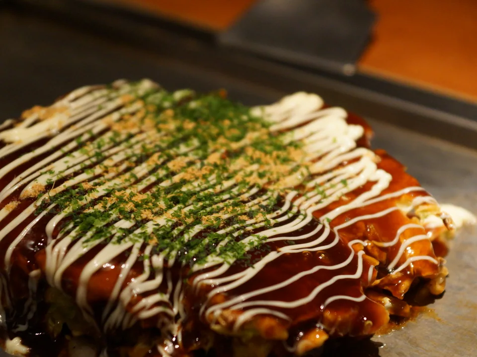 Osaka-style okonomiyaki topped with dark sauce, mayonnaise, aonori, and bonito flakes