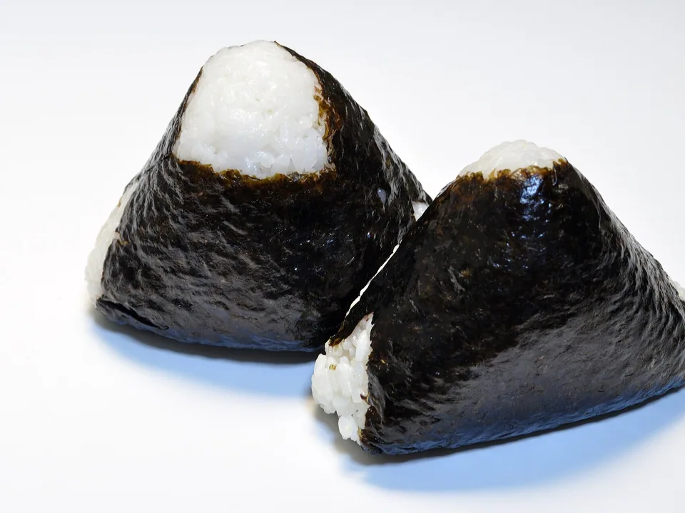 Real photograph of two plain triangular onigiri wrapped in broad sheets of black nori, with no visible filling or garnish.