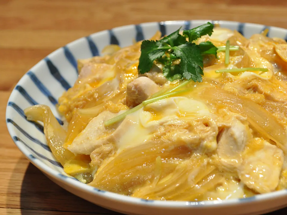 Soft egg and chicken oyakodon topping a bowl of white rice with mitsuba