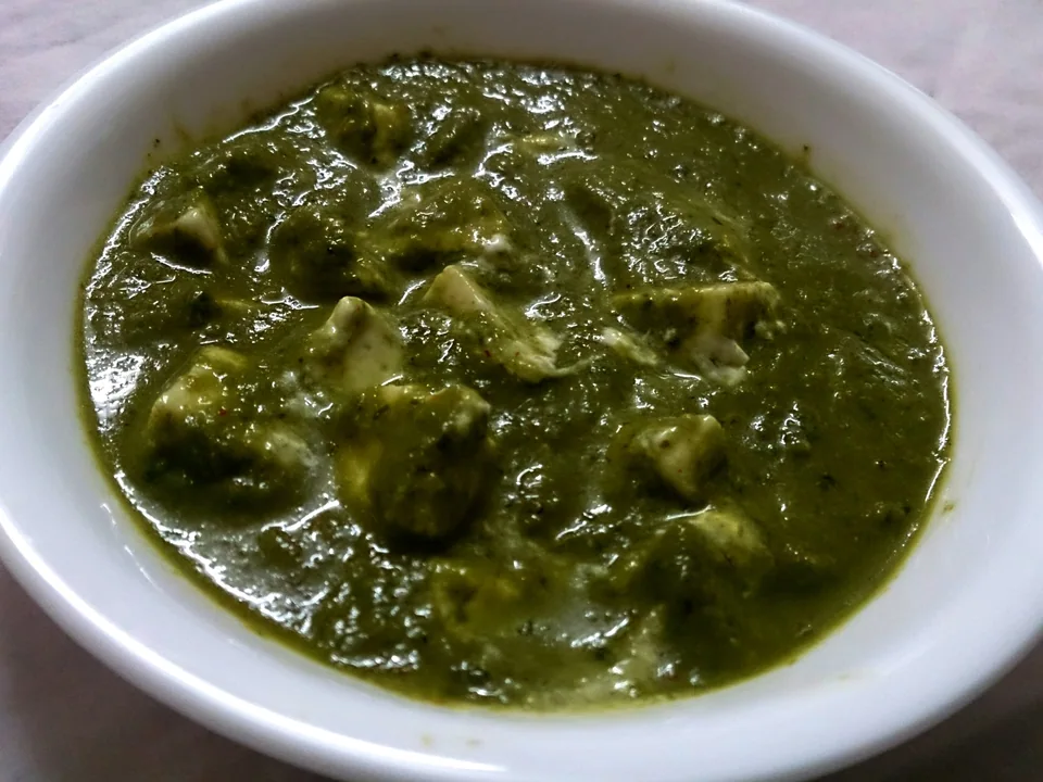 Palak paneer with white paneer cubes in vivid green spinach sauce and a restrained cream swirl