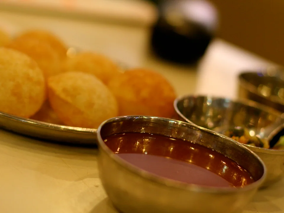 Crisp hollow pani puri filled with potato and chickpeas beside sweet chutney and cold green spiced water