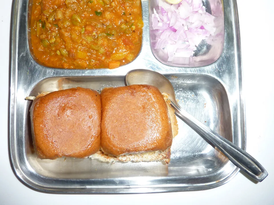 Mumbai pav bhaji with brick-red mashed vegetable curry, butter-toasted rolls, raw onion, cilantro, and lemon