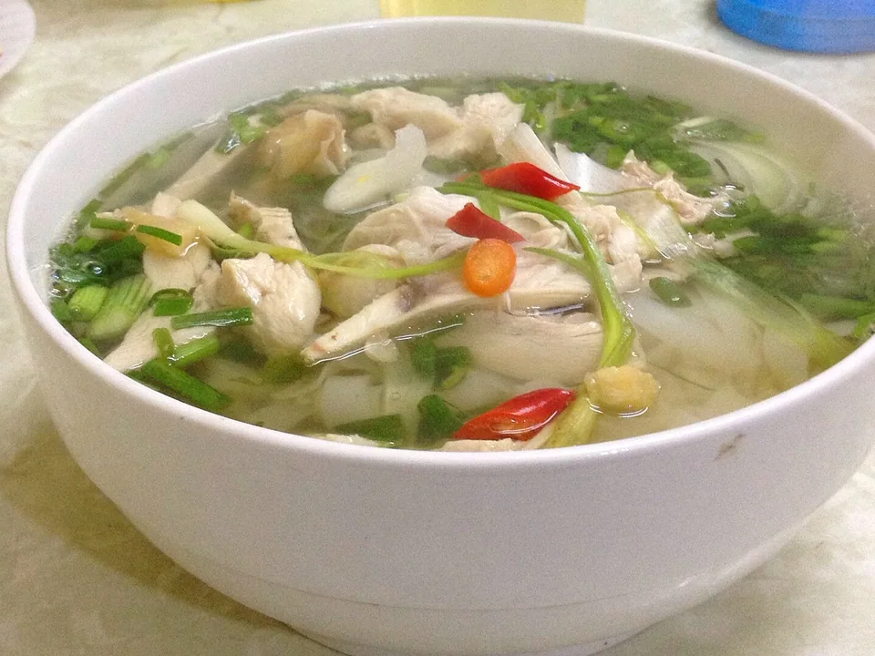 Chicken pho with pale sliced chicken and herbs in clear golden broth