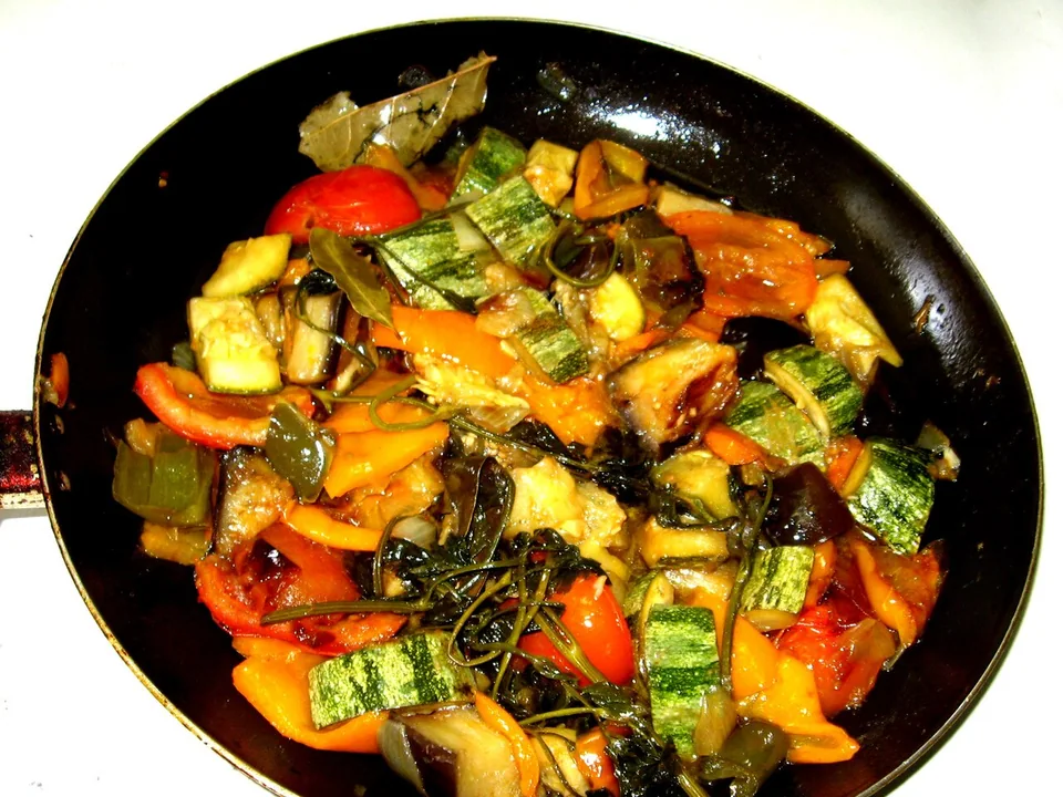 Chunky eggplant, zucchini, peppers and tomatoes with herbs in a dark pan