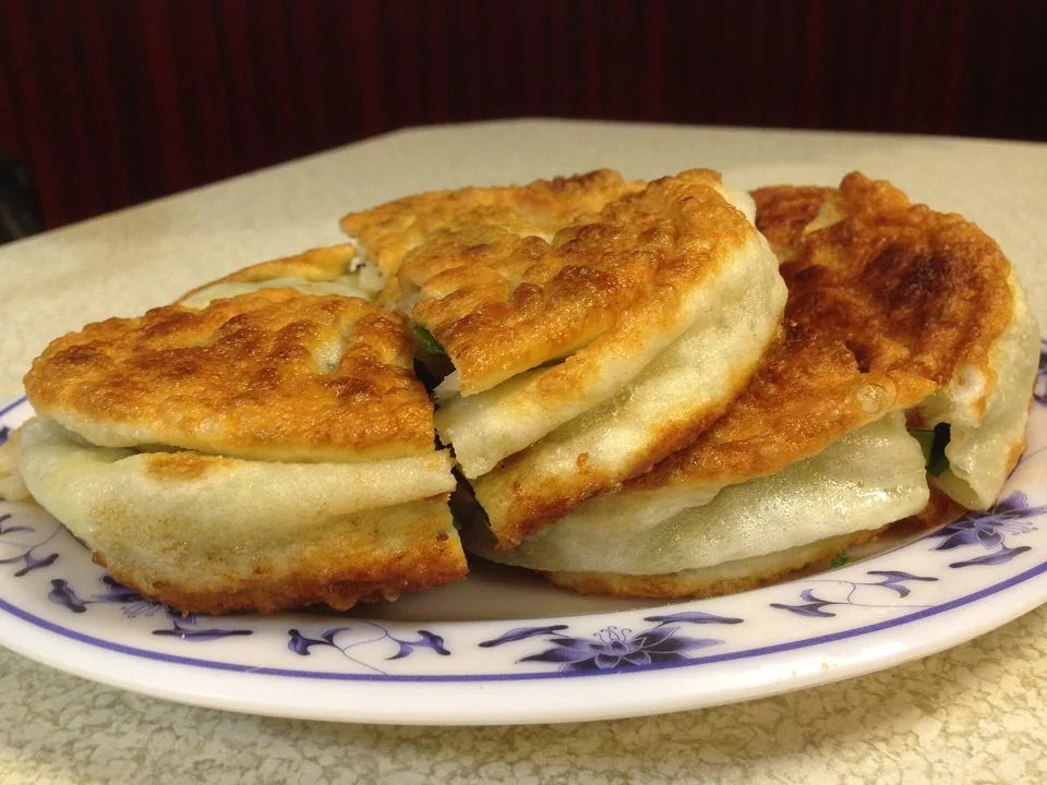 Golden scallion-pancake wedges stacked on a plate, with crisp blistered surfaces, flaky layers, and green scallion at the cut edges
