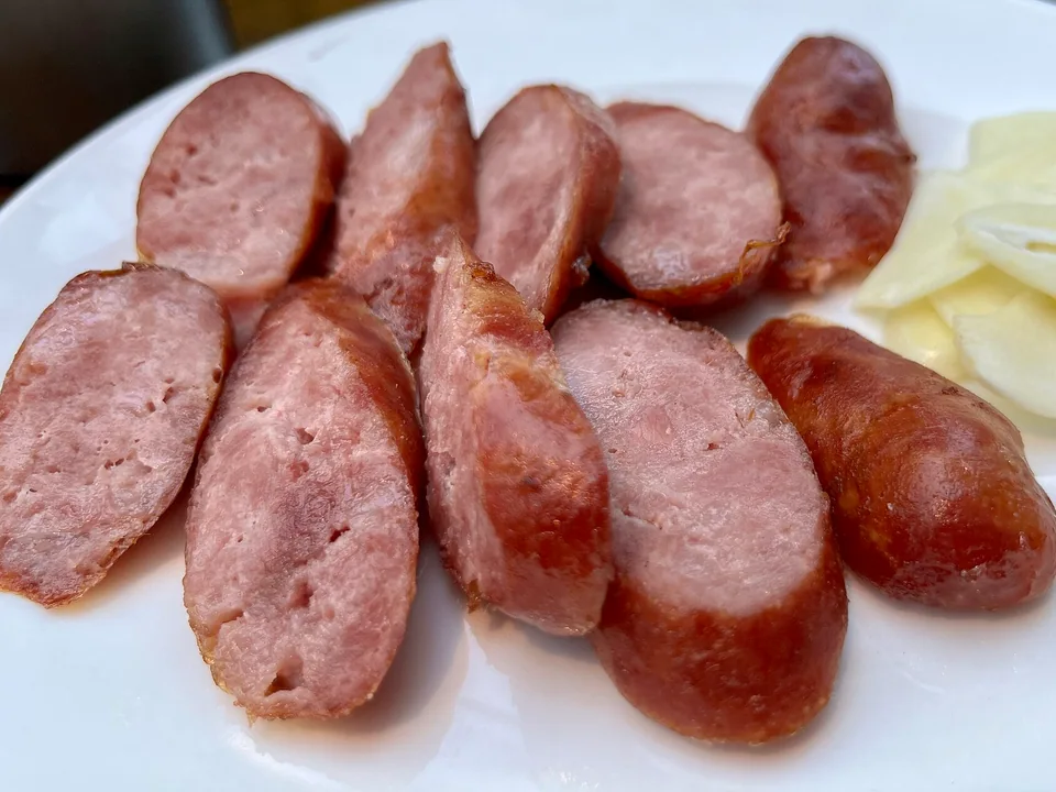 Sliced glossy Taiwanese pork sausage with browned casing, coarse filling, and raw garlic slices