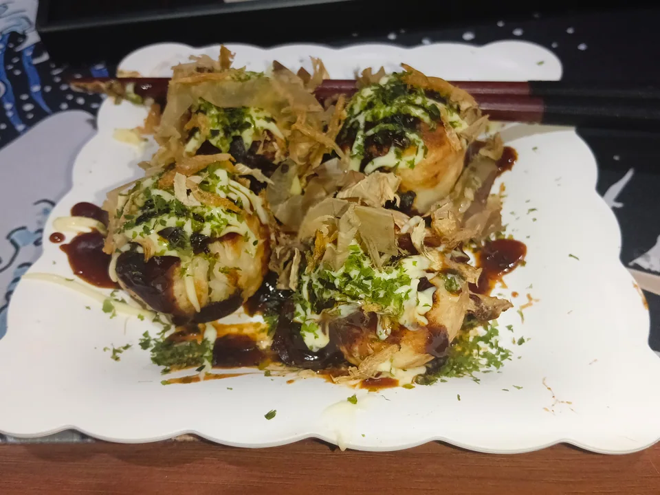 Takoyaki balls topped with dark sauce, Japanese mayonnaise, aonori, and bonito flakes on a white plate