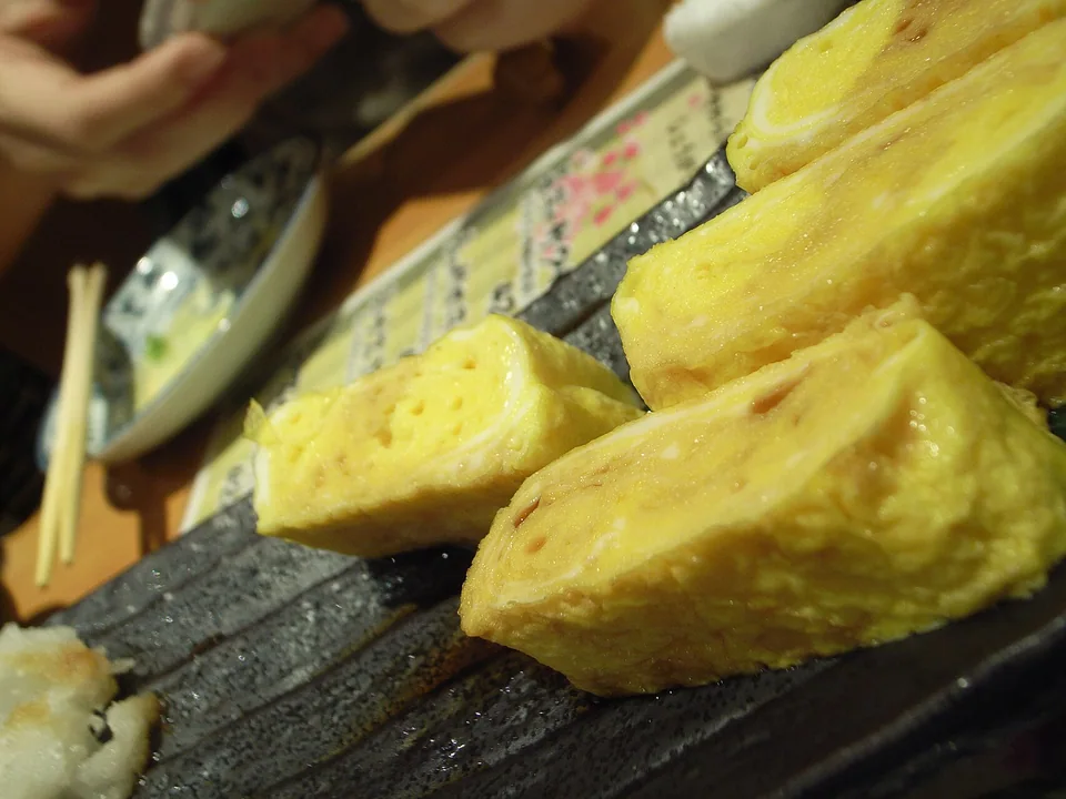Real photograph of plain yellow tamagoyaki cut into thick layered pieces, with no visible garnish or filling.