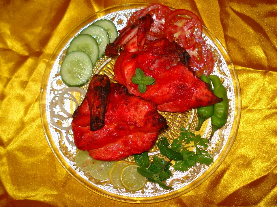 Charred red-orange tandoori chicken legs with mint chutney, sliced onion, and lemon