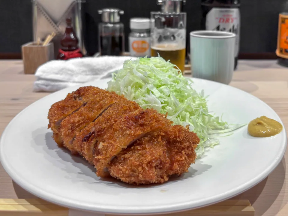 Sliced golden tonkatsu with shredded cabbage and yellow mustard on a white plate