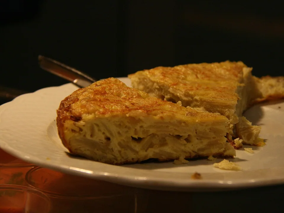 Thick golden Spanish tortilla with visible potato layers in a cut wedge