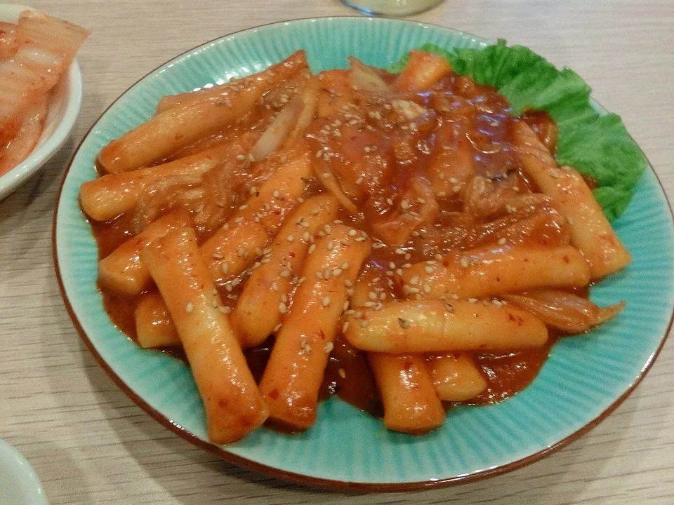 Glossy red tteokbokki with cylindrical rice cakes, fish cake, and scallions