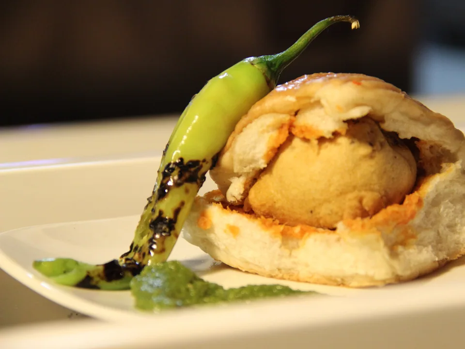 Mumbai vada pav with a golden potato fritter, dry garlic chutney, and green chutney in a soft roll